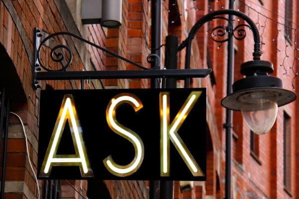 A neon sign that says ask hanging from the side of a building.