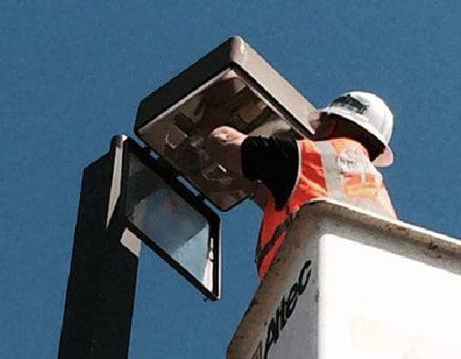 A man in an orange vest is on top of a white pole.