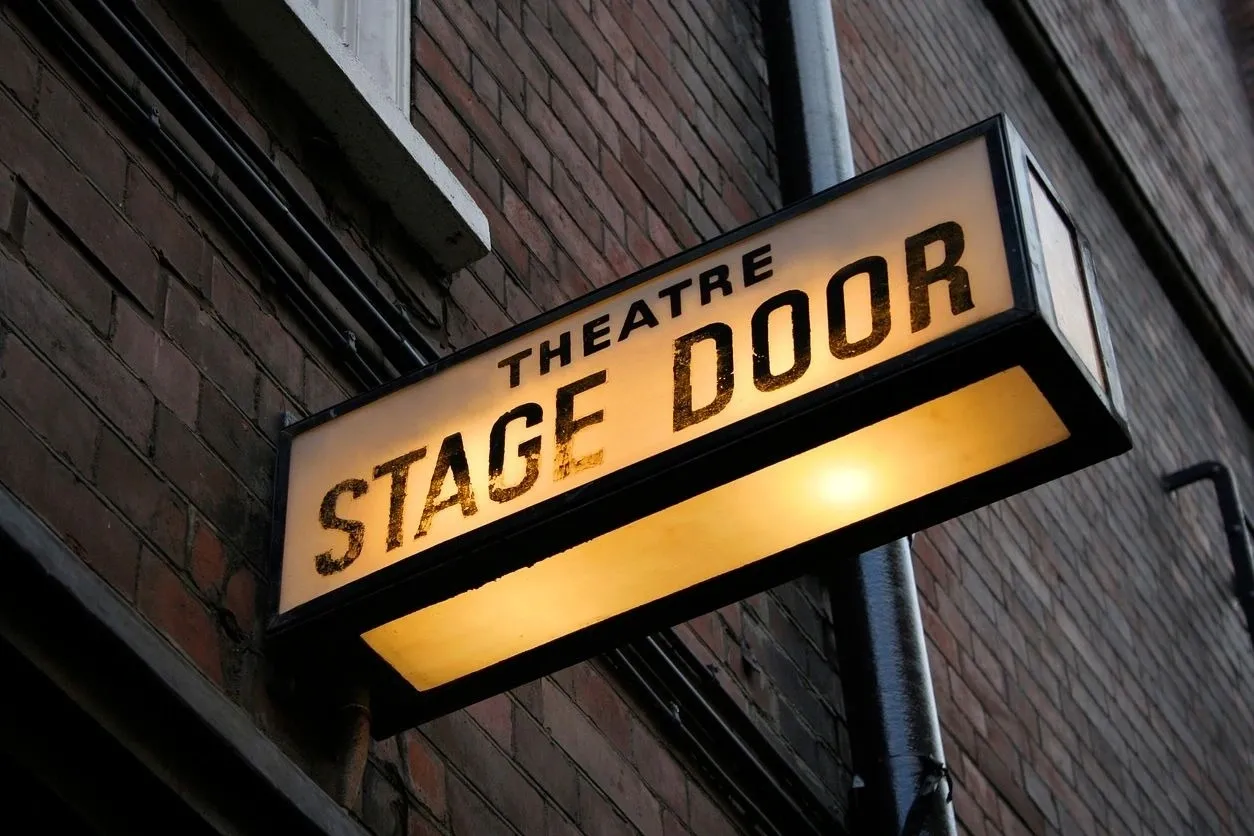 A theatre stage door sign hanging from the side of a building.